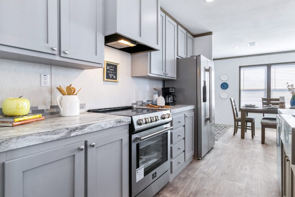 Kitchen with gray cabinets, marble countertop, stainless steel appliances, and a dining area with a table and chairs by a window.