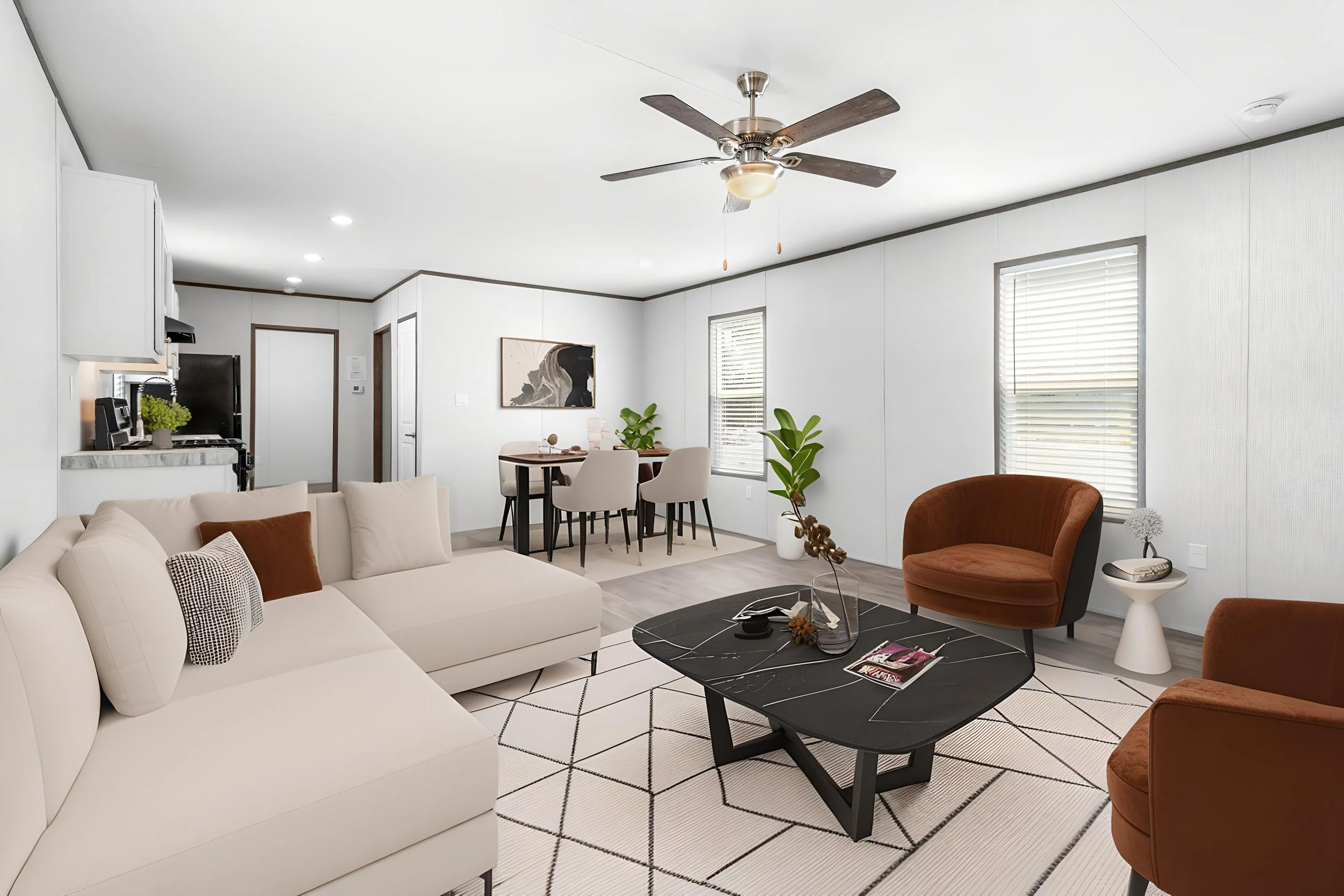 Living room with white sofa, brown armchair, black coffee table, white walls, and windows with blinds. Dining area with round table and four chairs. Ceiling fan with light. Artwork on wall, plants, and decorative items.