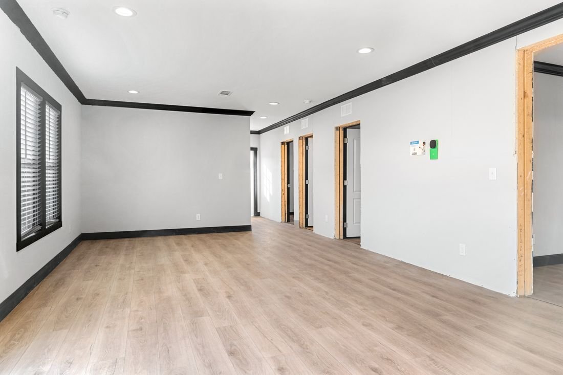 Empty room with light wood flooring, white walls with black trim, three door openings, and window blinds.