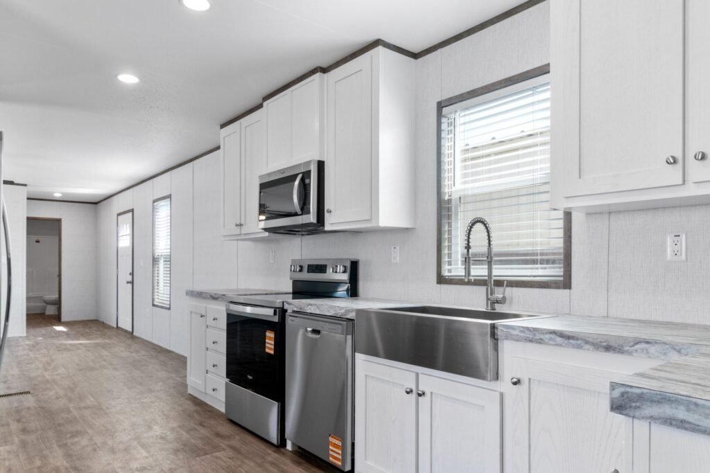 Modern kitchen with white cabinets, stainless steel appliances, marble countertops, and a large farmhouse sink.