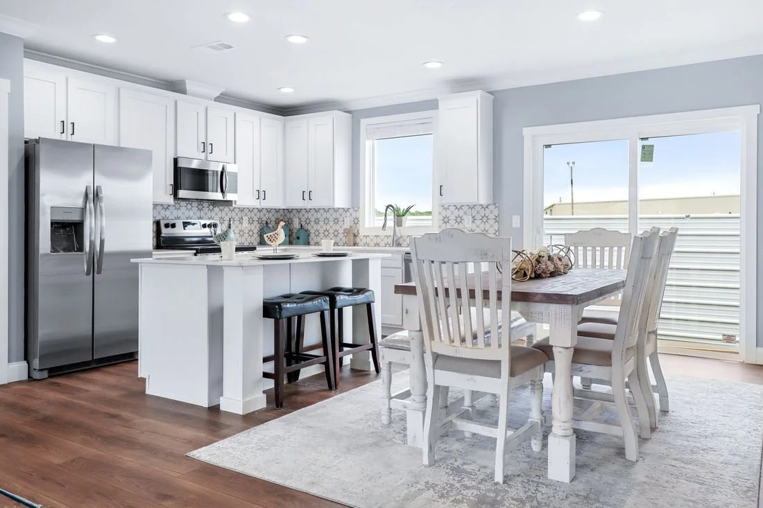 Modern kitchen with white cabinets, stainless steel appliances, and a dining area with a wooden table and white chairs.