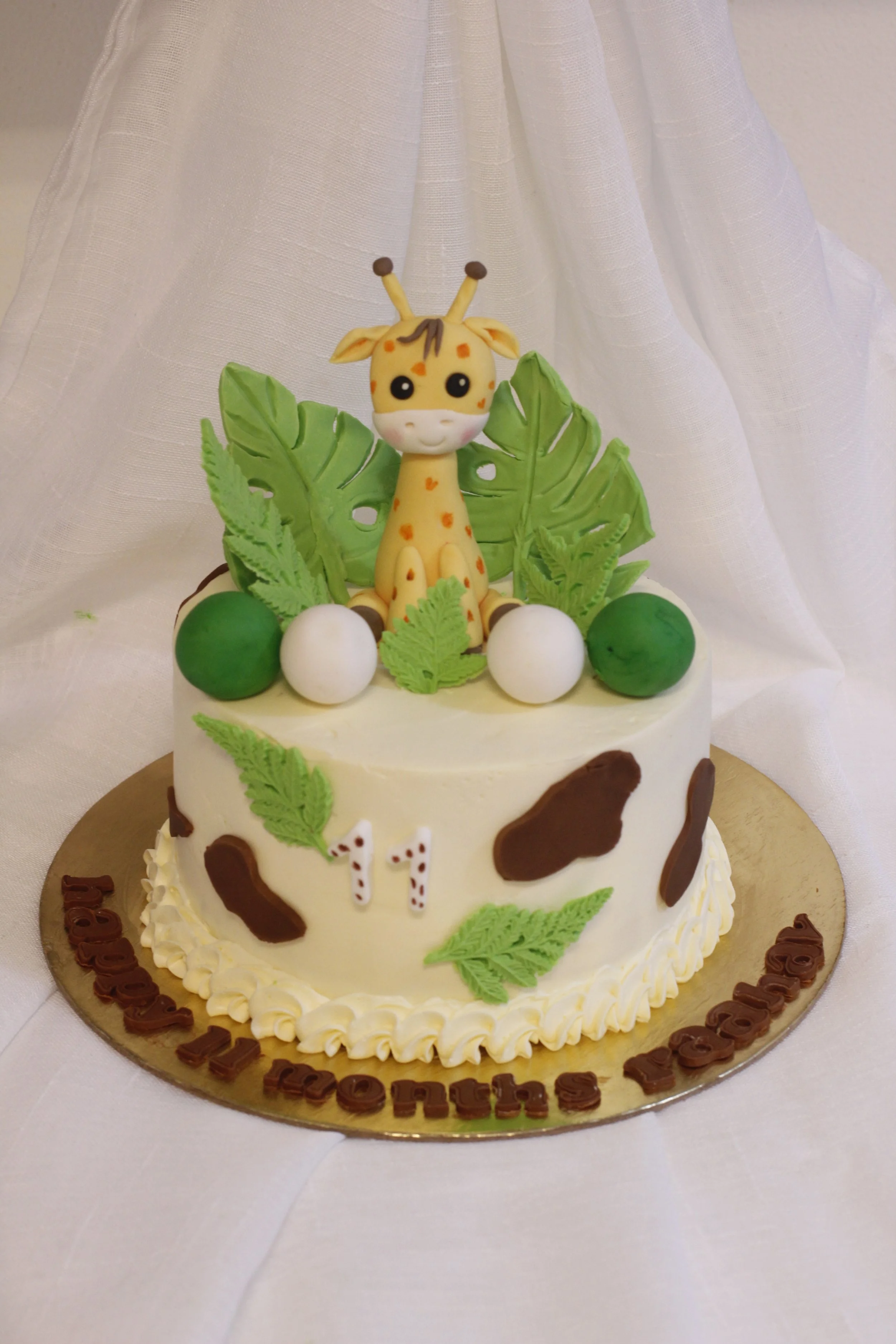 A birthday cake with a giraffe topper, green leaves, and white and green spherical decorations, with a 