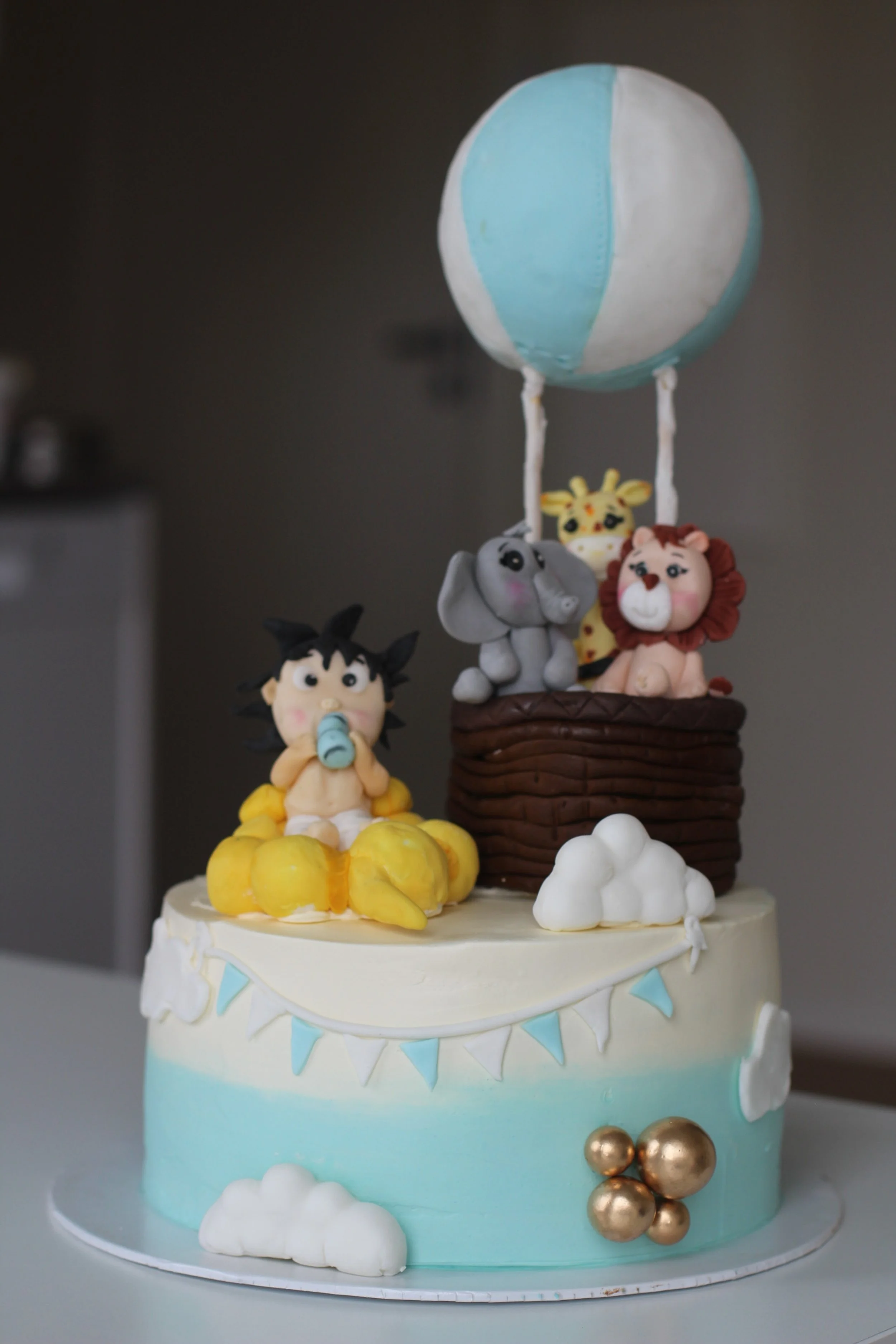 A jungle animal-themed cake with figurines of a boy, elephant, lion, giraffe, and monkey, with a hot air balloon topper