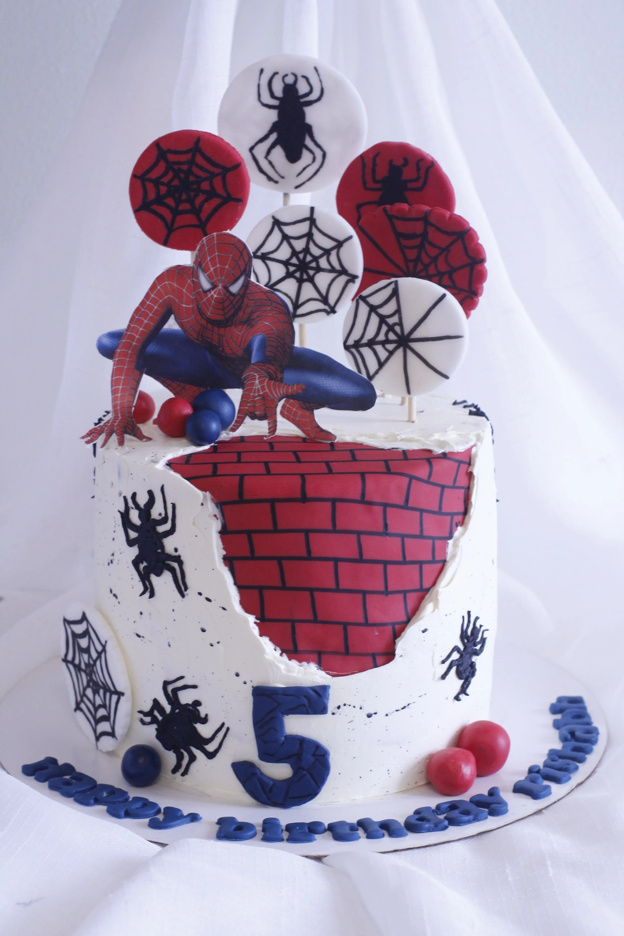 Spiderman themed birthday cake with spider web decorations, Spiderman figure, and colored balls, celebrating a 5th birthday.