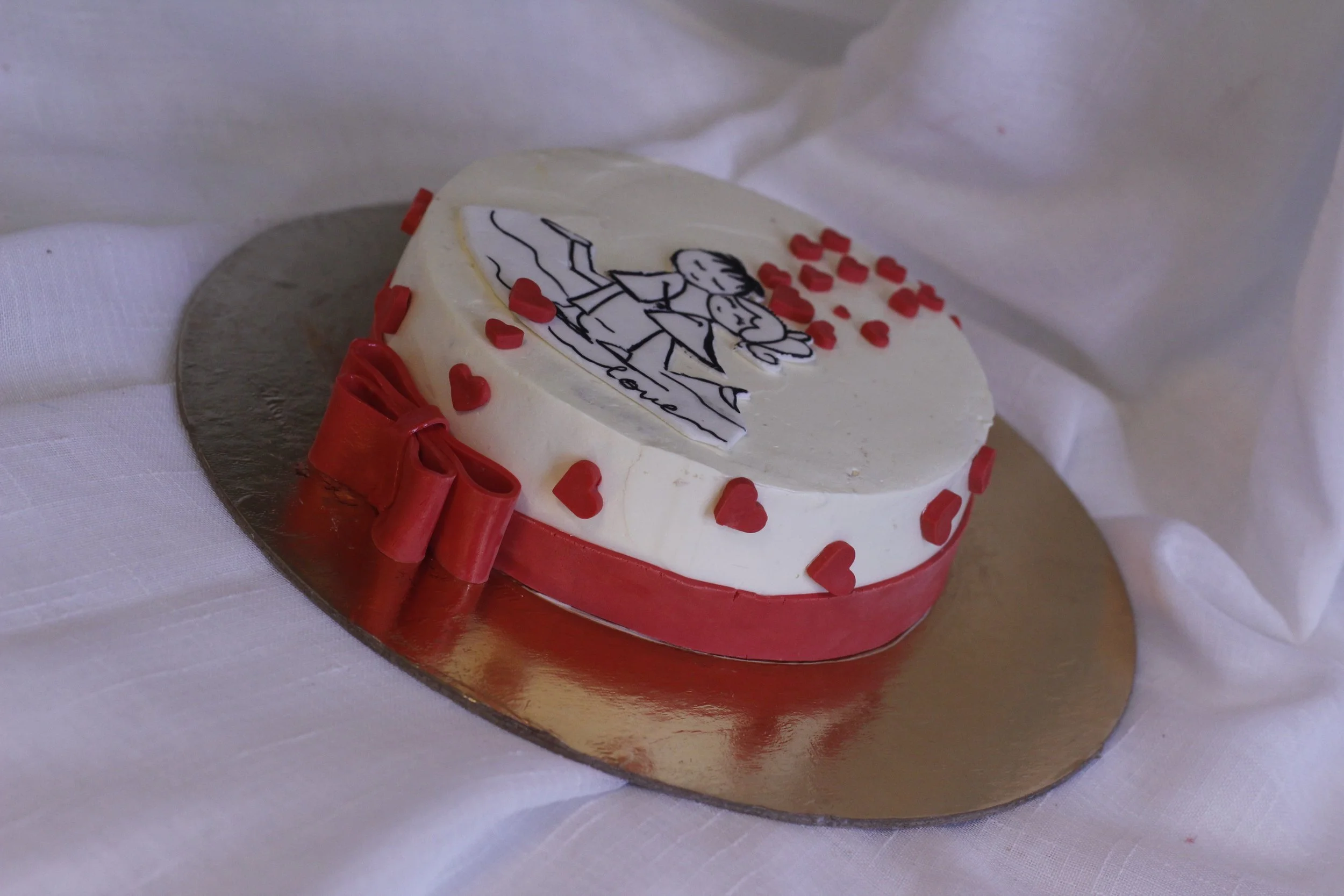 Heart-shaped white cake decorated with red hearts and a red bow, featuring an edible image of a couple holding hands with the word 'love'.