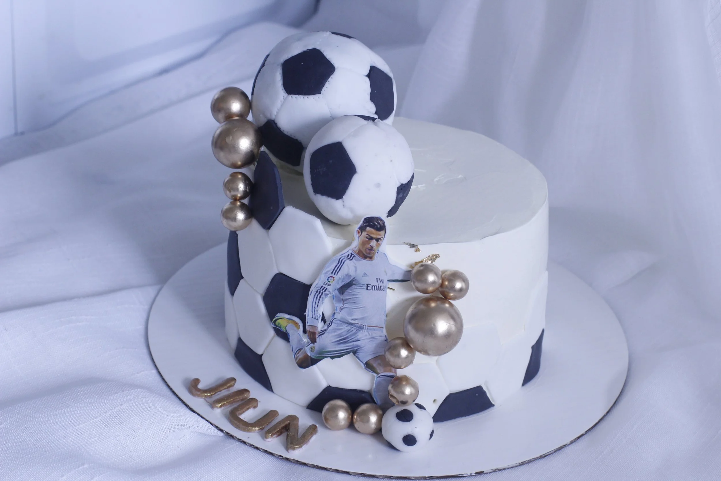 A soccer-themed cake decorated with soccer balls, gold spheres, and an image of Cristiano Ronaldo in his Real Madrid kit.