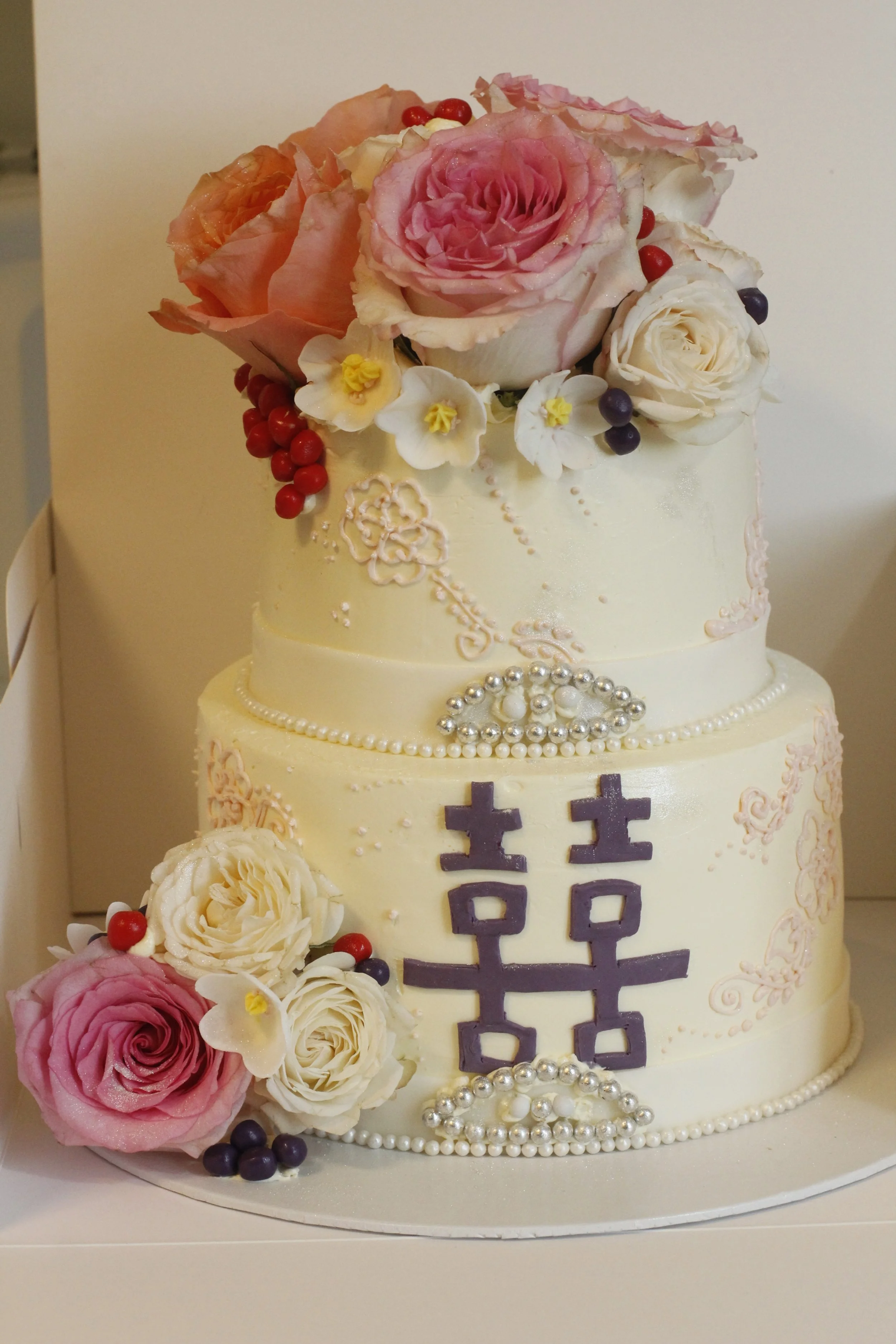 Two-tier wedding cake decorated with flowers, pearls, and Chinese characters for double happiness.