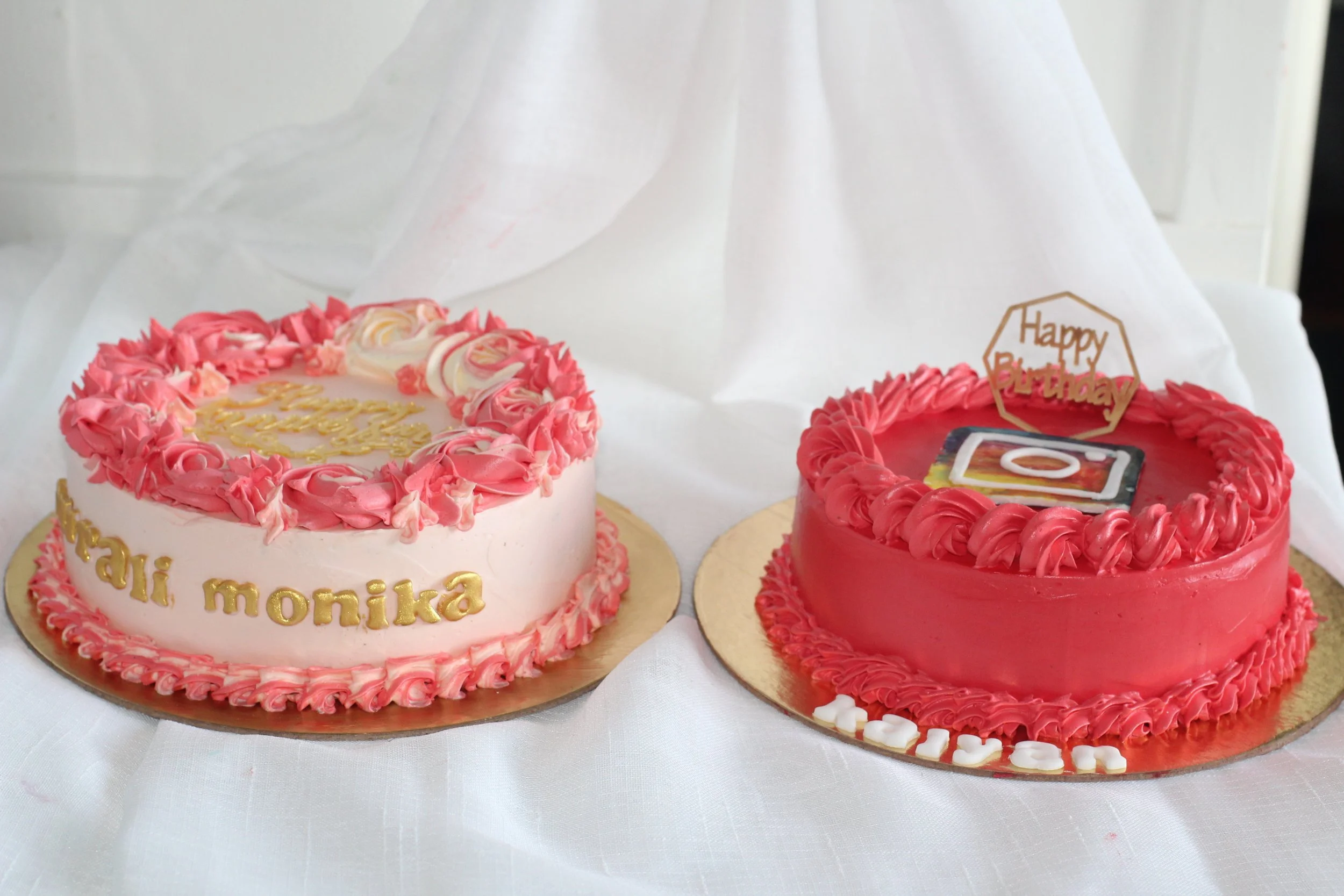 Two decorated birthday cakes, one pink with gold lettering and pink frosting, the other red with a photo of a phone and a small "Happy Birthday" topper.