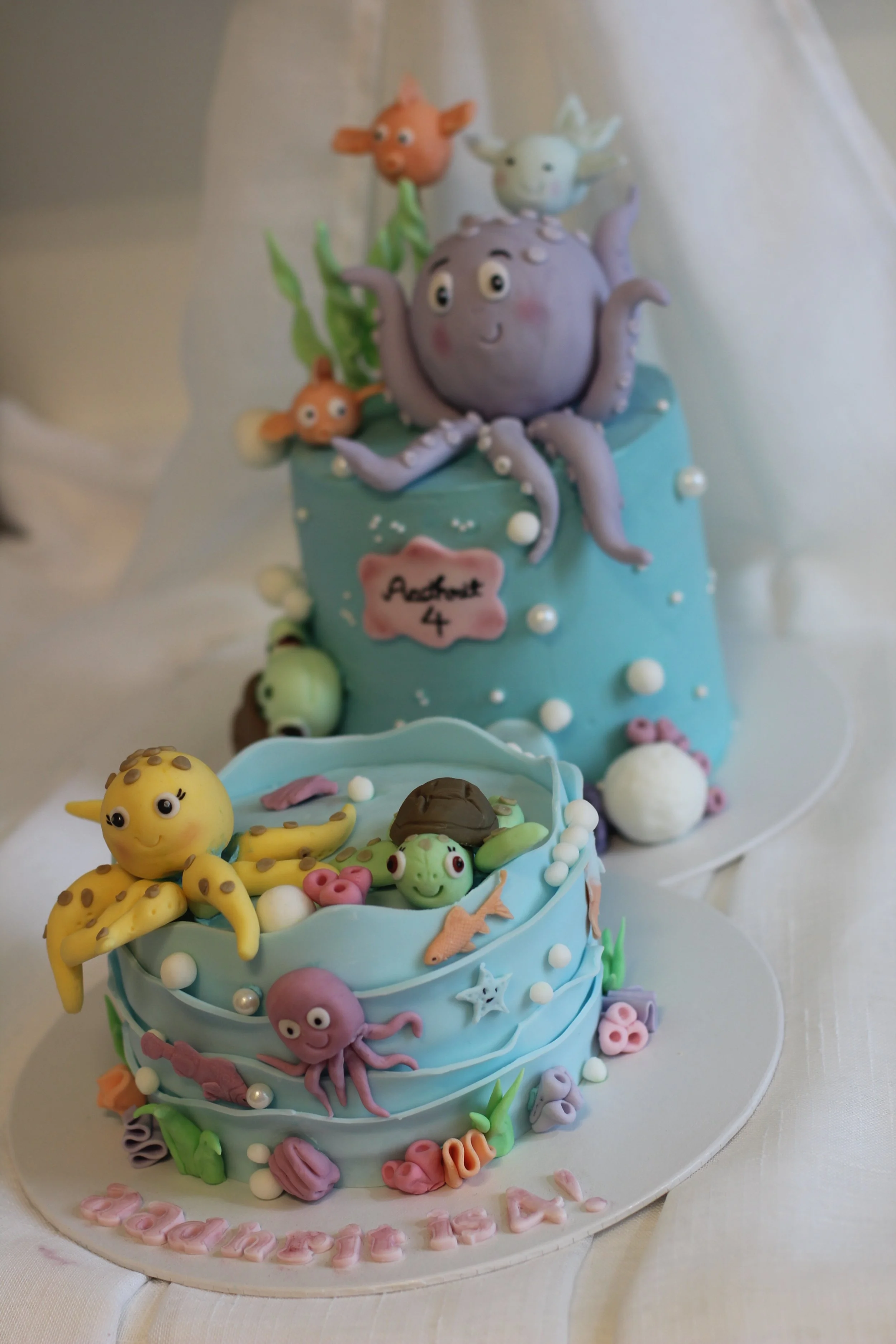 A decorated birthday cake with an underwater theme, adorned with fondant sea creatures like an octopus, frog, sharks, and fish, over two tiers, with 