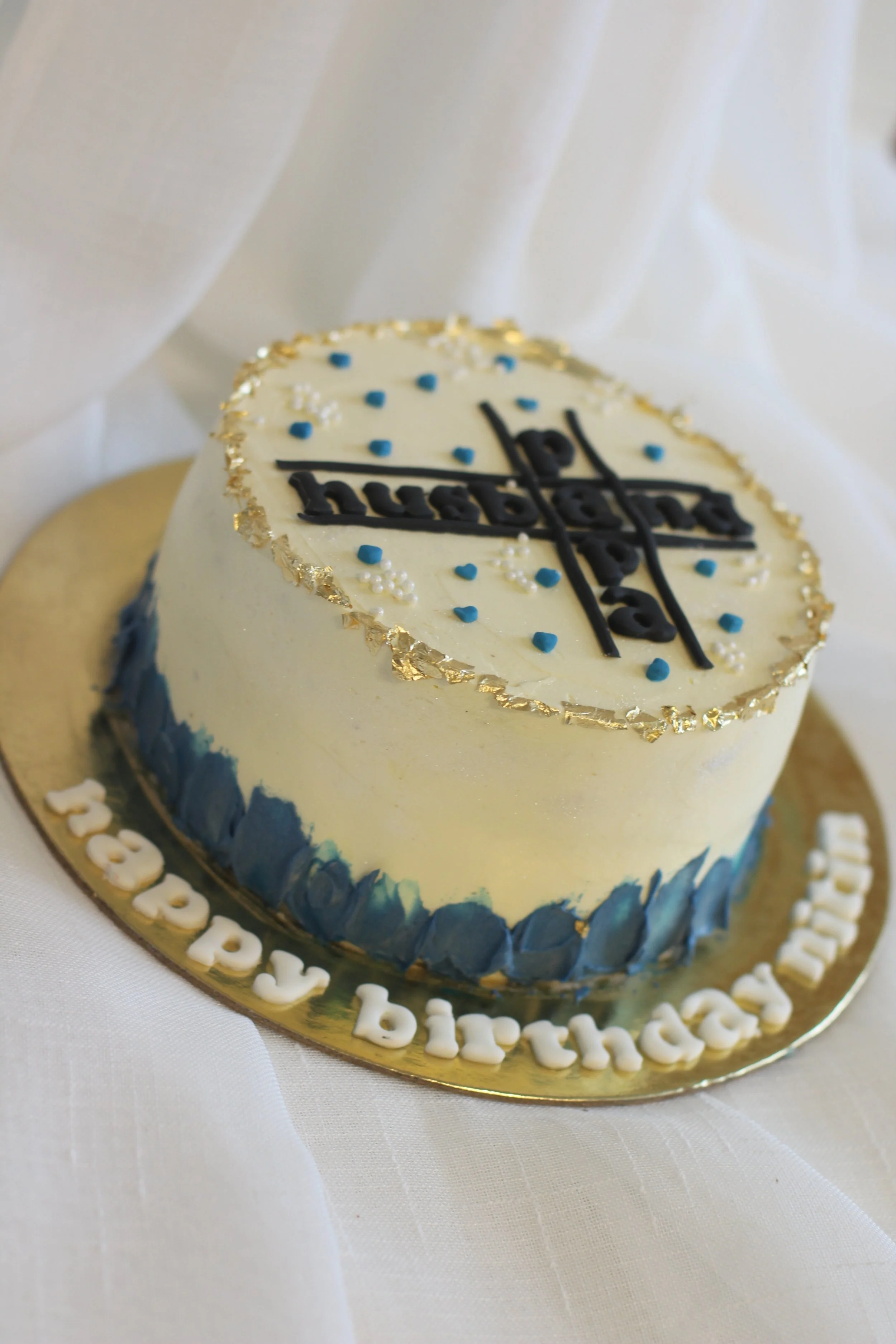 A cake with white and blue icing, decorated with gold accents, birthday message, and topped with the BlackBerry logo.