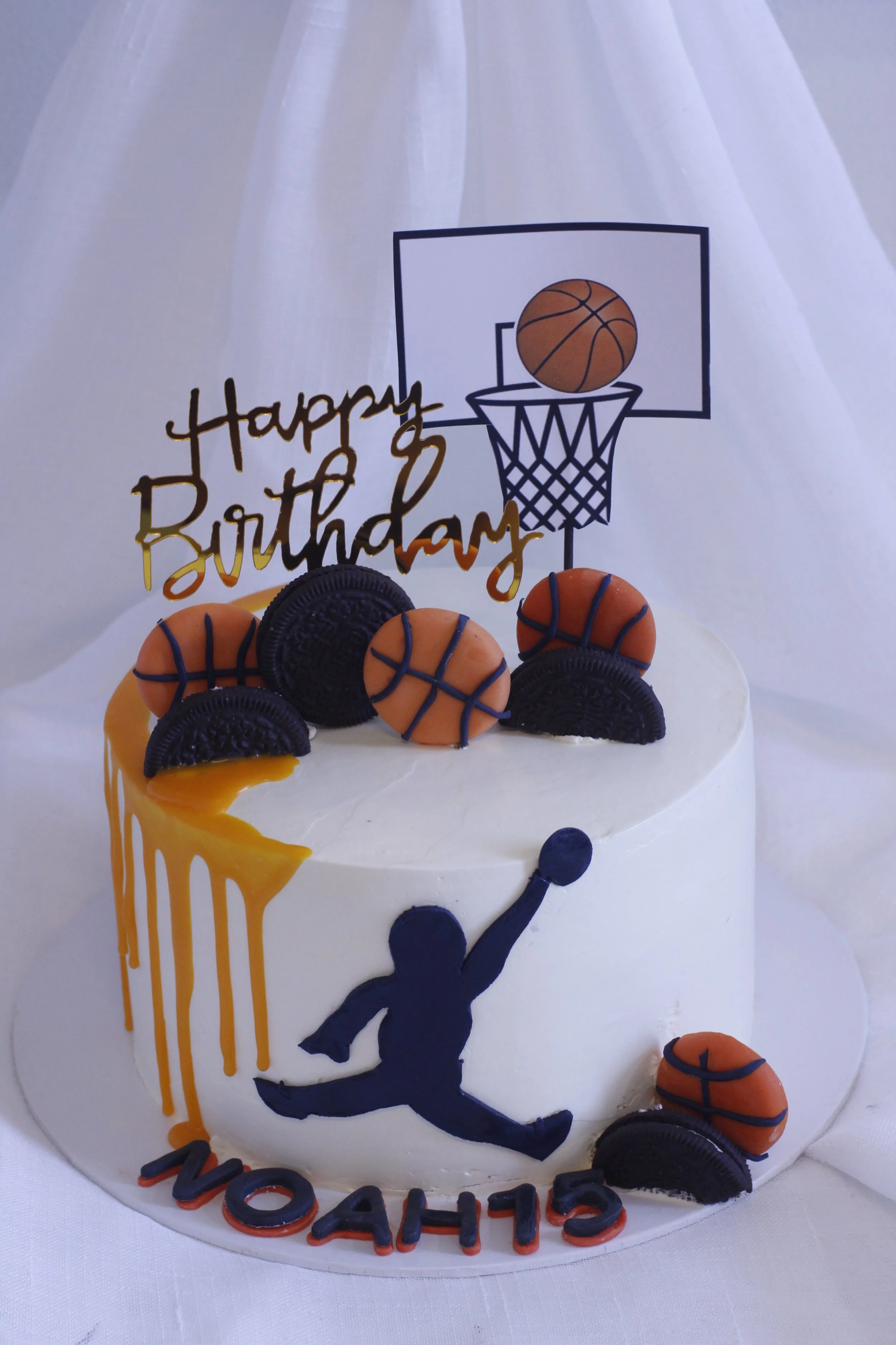 A basketball-themed birthday cake decorated with basketball cookies, Oreos, a silhouette of a basketball player, a basketball hoop topper, and a "Happy Birthday" sign, with the name "Shayoh" and the number "15" on the cake.