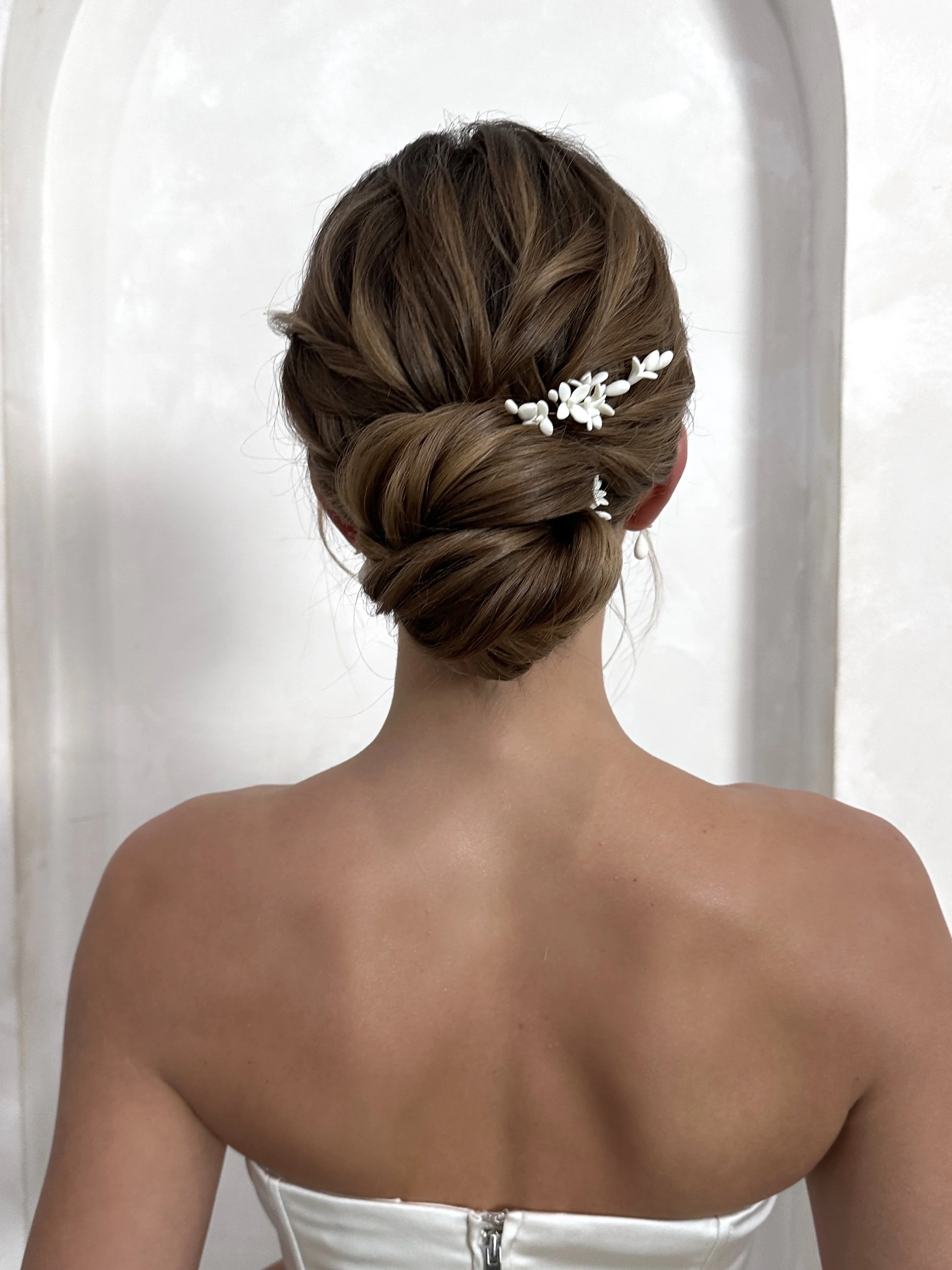 Back view of a woman with an elegant updo hairstyle decorated with white floral hair accessories.