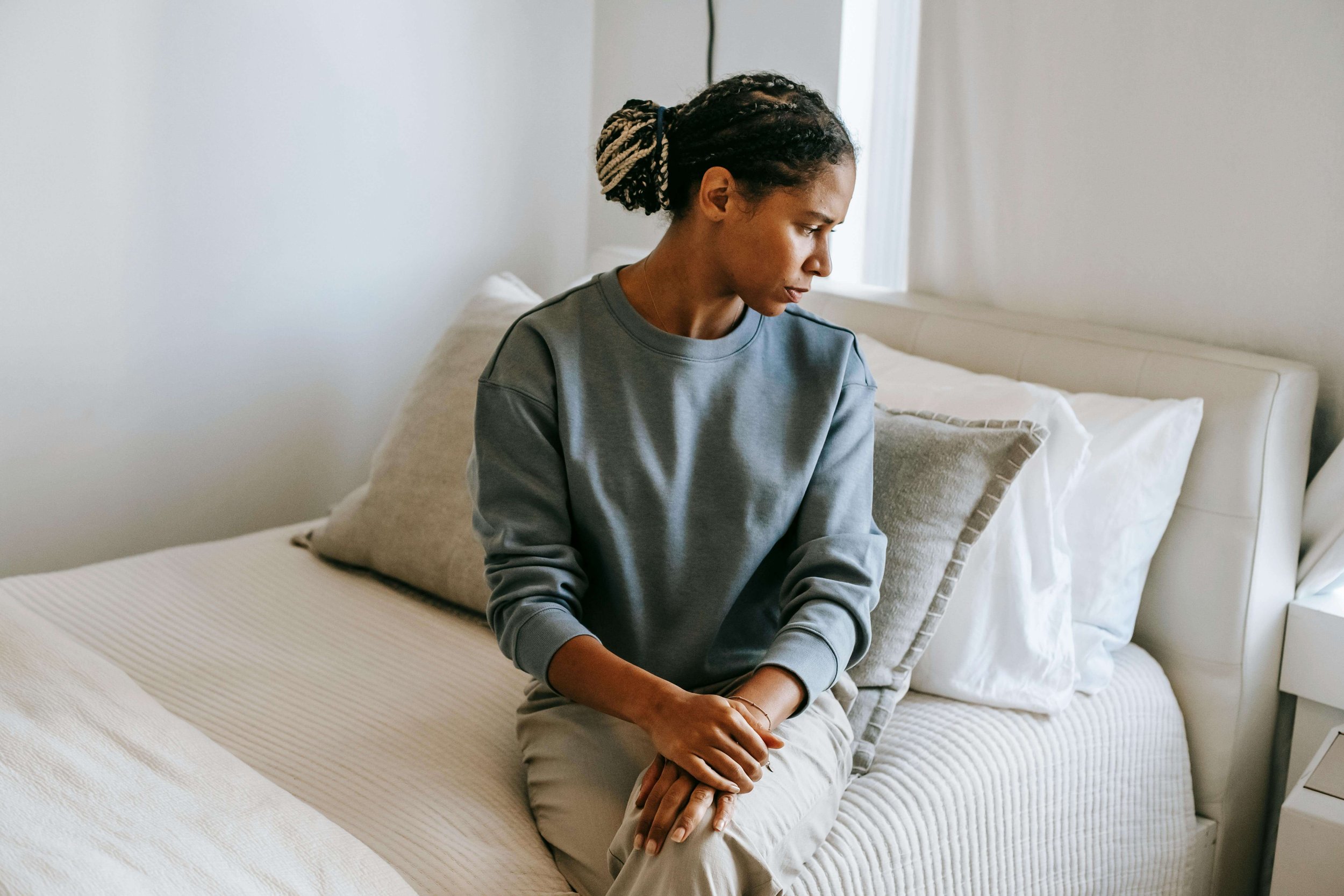 Person sitting on a bed with a solemn expression, portraying the loneliness and sadness that can lead someone to seek grief counseling in Sacramento, CA.