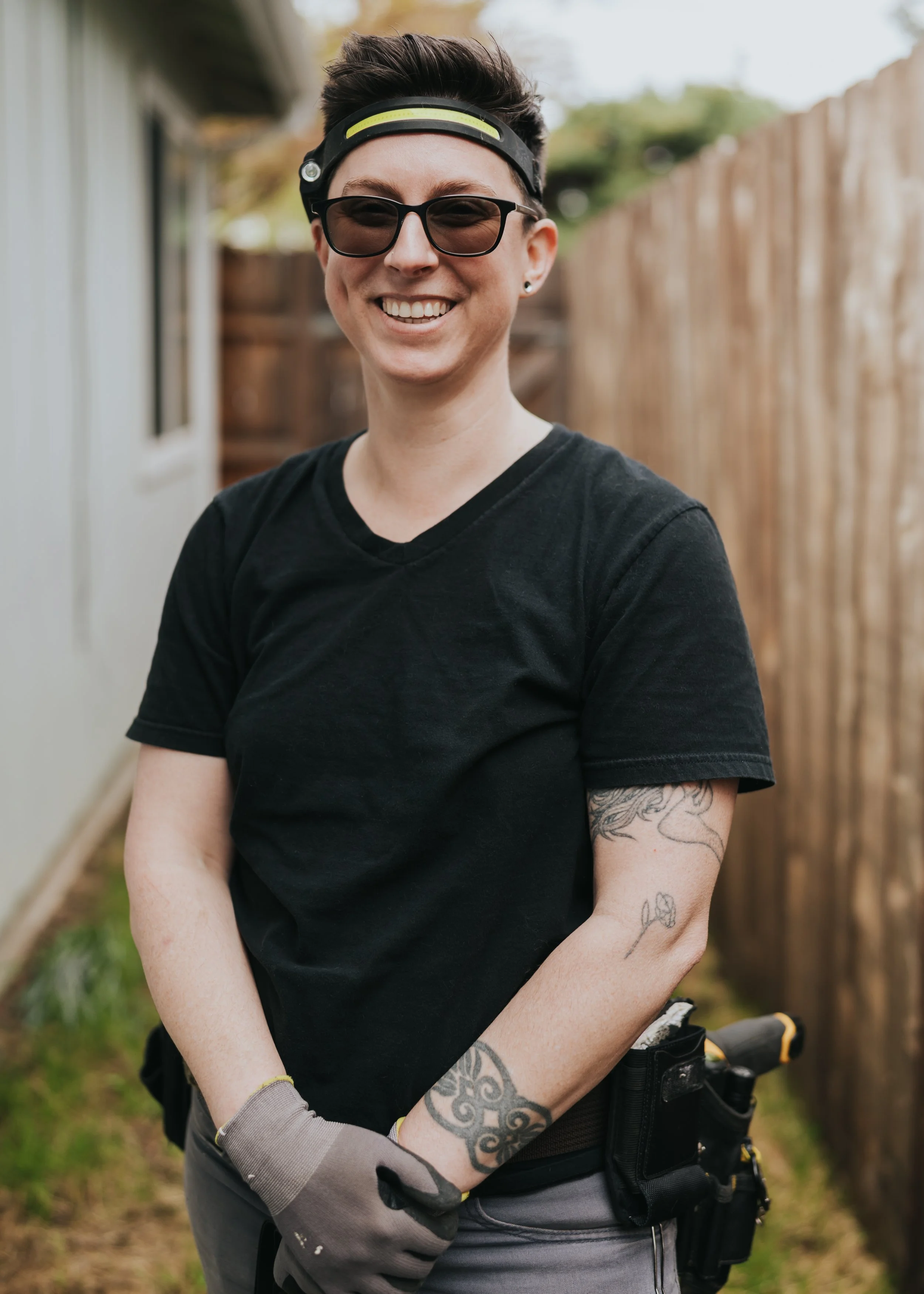 Marissa Longpeak, inspector is wearing work gloves and a utility belt, standing outdoors in a backyard with a wooden fence.