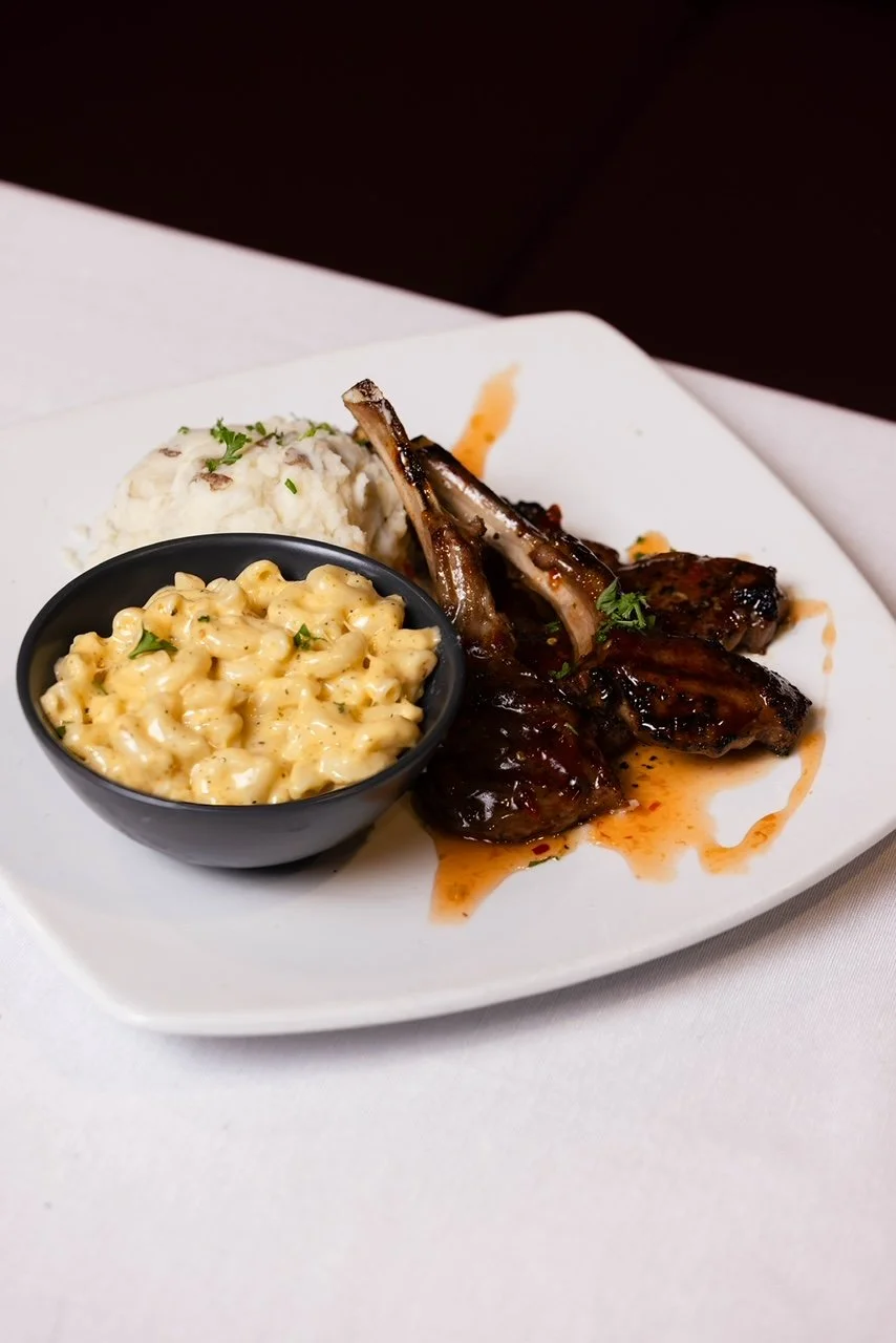 Plate of grilled lamb chops with barbecue sauce, served with mashed potatoes, macaroni and cheese, and a side of potato salad