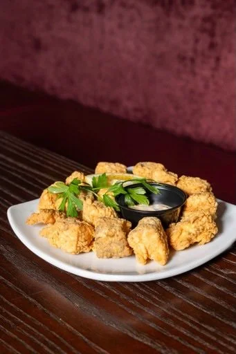 Plate of fried chicken nuggets with a small bowl of dipping sauce and a sprig of parsley