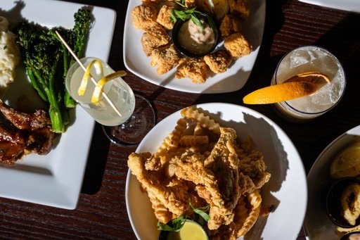 Fried chicken wings, broccoli with lemon, and drinks including a lemon cocktail and a soda on a dark wooden table.
