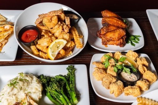 Assorted Asian dishes including fried chicken, fried fish, broccoli with mashed potatoes, and fried calamari with dipping sauce on white plates.