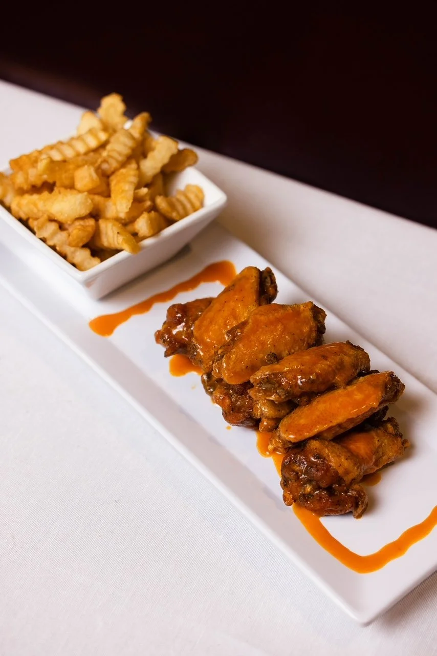Buffalo chicken wings with a side of waffle fries served on a long white platter