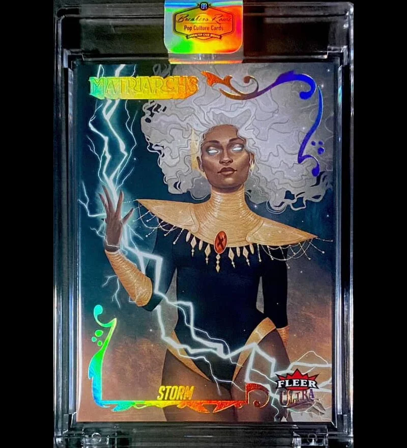 Holographic trading card featuring a woman with glowing white hair and mystical expression, dressed in black and gold costume, with lightning effects surrounding her hand, labeled 'Storm' from the 'Marvel Comics' series.