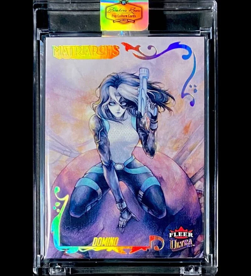 A Marvel trading card titled 'Matriarchs' featuring a female character with long hair holding a gun, sitting on a round object with a pastel-colored background. The card is encased in a plastic protective sleeve.