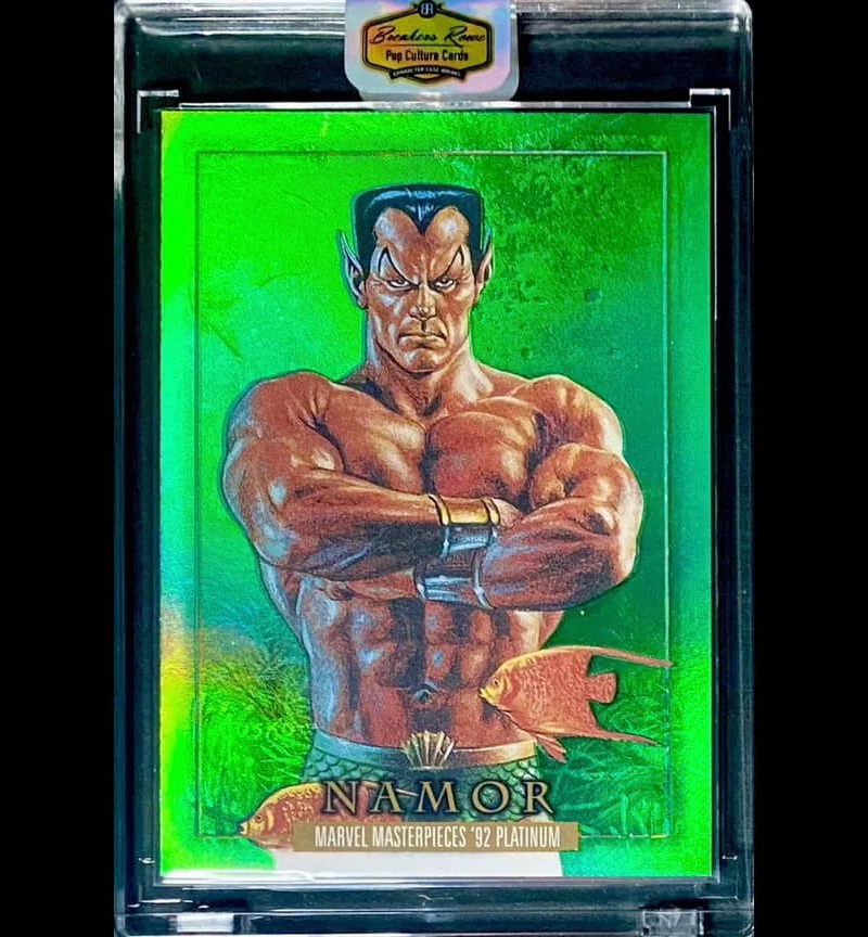 A holographic trading card featuring Namor, a muscular superhero with crossed arms, dark hair, and a serious expression, set against a green background with two orange fish and a title indicating Marvel Masterpieces '92 Platinum.