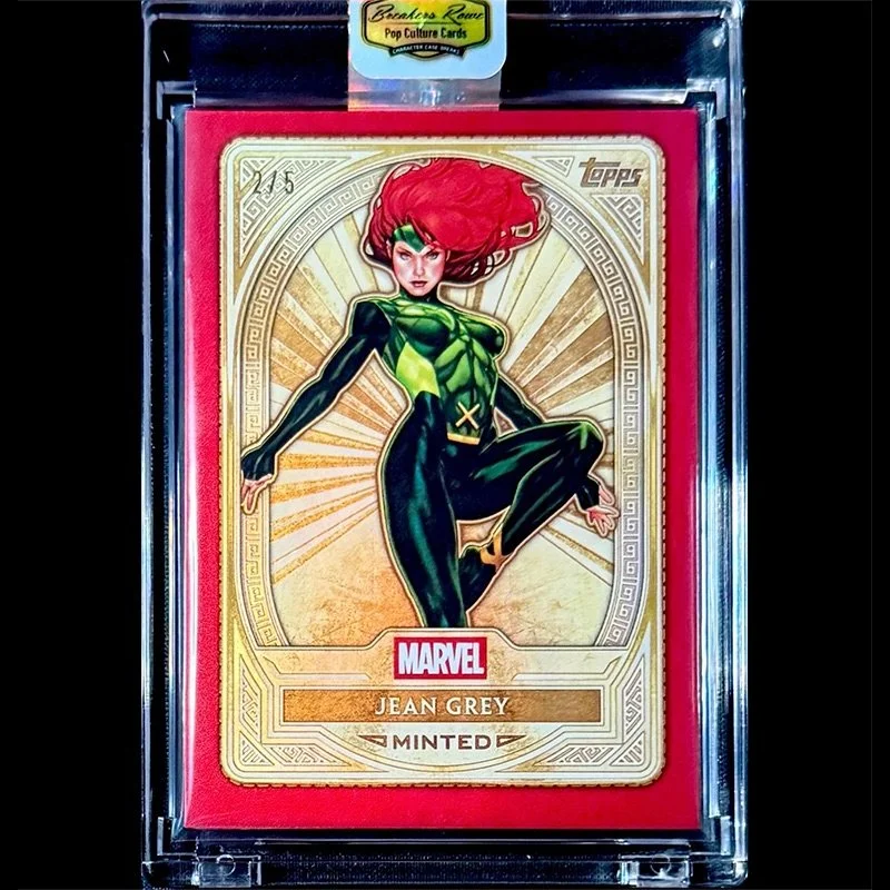 A collectible card of Marvel's Jean Grey in a protective case, featuring a colorful illustration of her with red hair and a green and black costume, mounted on a red background.