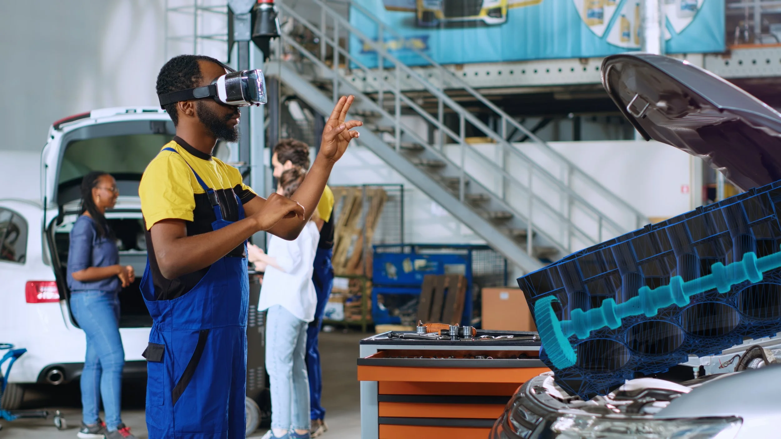 A man wearing a yellow shirt, blue overalls, and a virtual reality headset appears to be inspecting or demonstrating an engine in an auto repair shop. Other people are in the background, engaging in activities near an open car trunk, with workshop tools and equipment present.