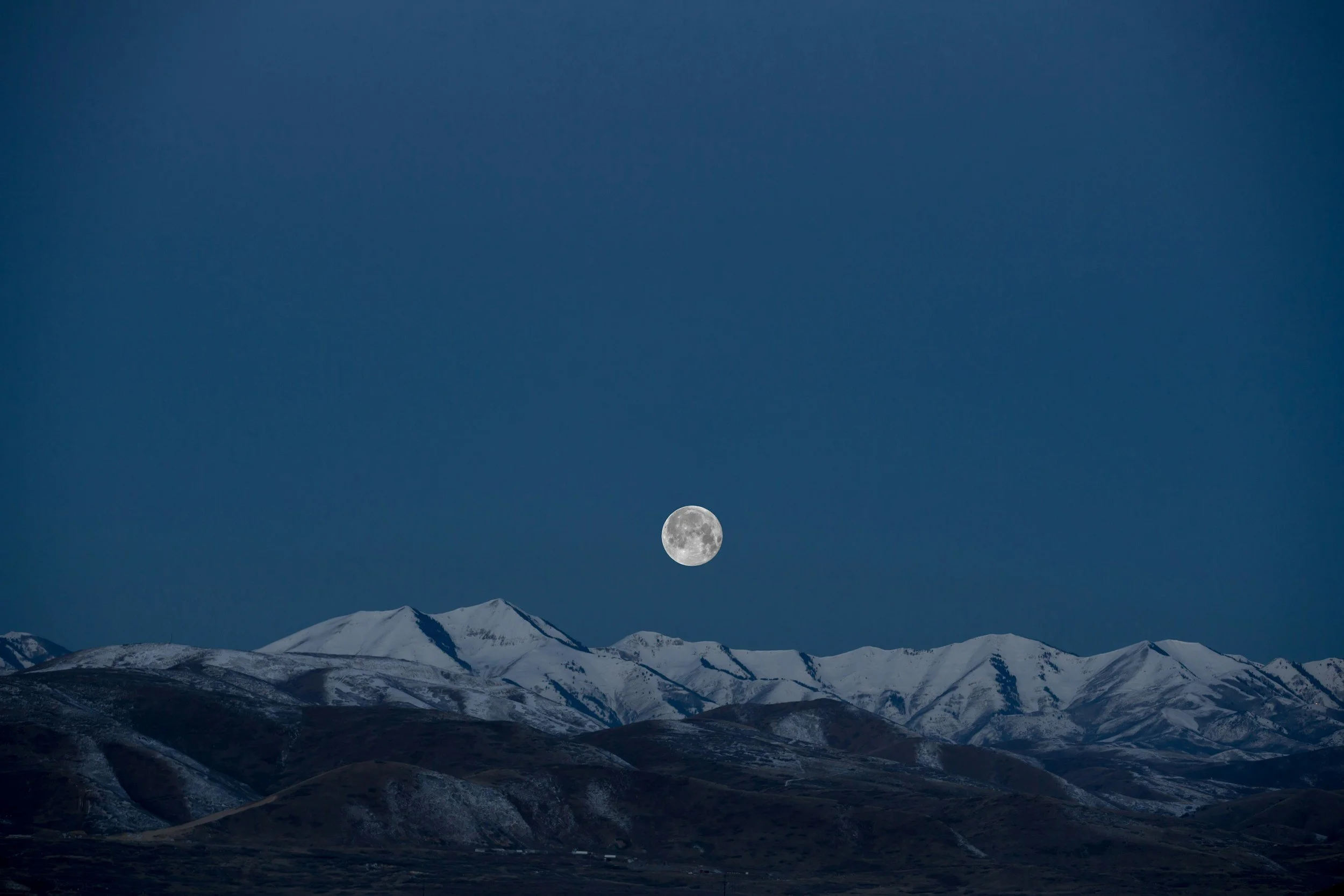 Night sky with full moon over snow-capped mountains.
