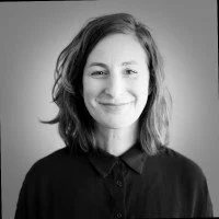 Retrato en blanco y negro de una mujer con cabello castaño, sonrisa y ropa oscura.