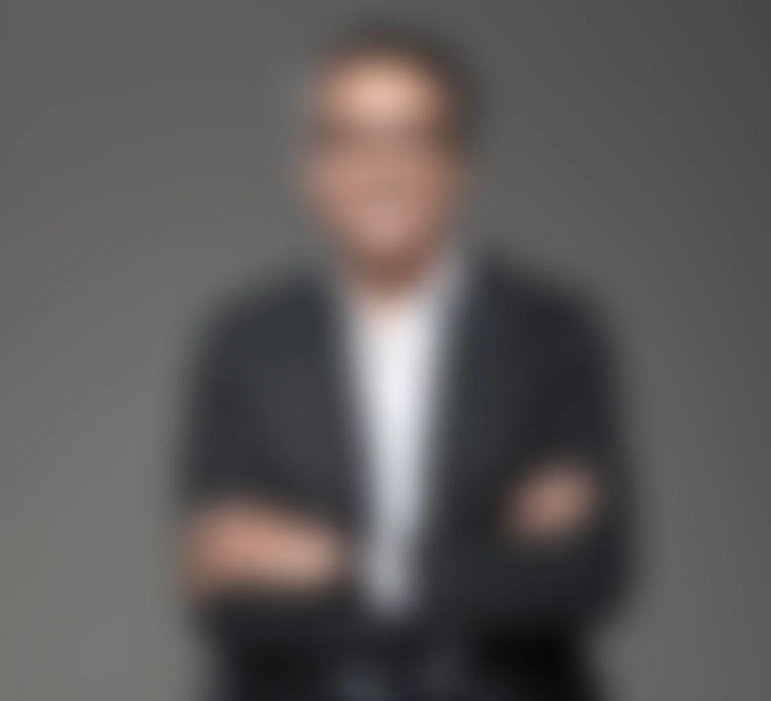 Persona de negocios con traje oscuro y brazos cruzados, con fondo gris.