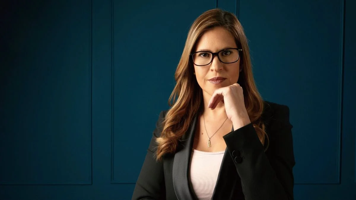 Persona con cabello largo y rostro difuso, vestida con ropa oscura, en un fondo azul.