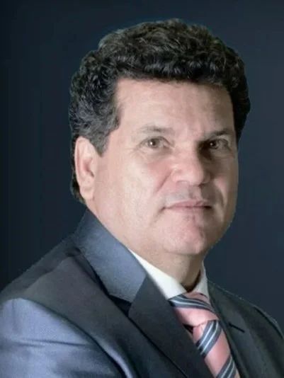 Retrato de un hombre de cabello rizado oscuro, ropa formal con saco, camisa y corbata, fondo oscuro.