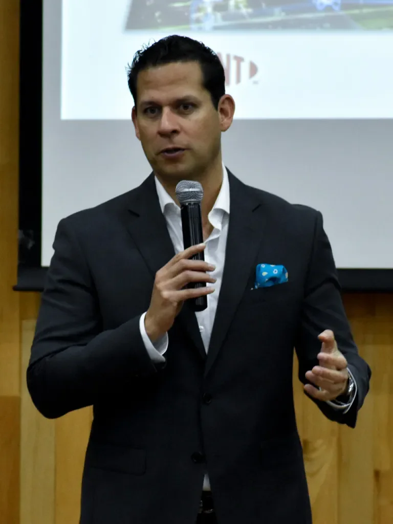 Hombre de traje hablando con micrófono en una presentación o conferencia.