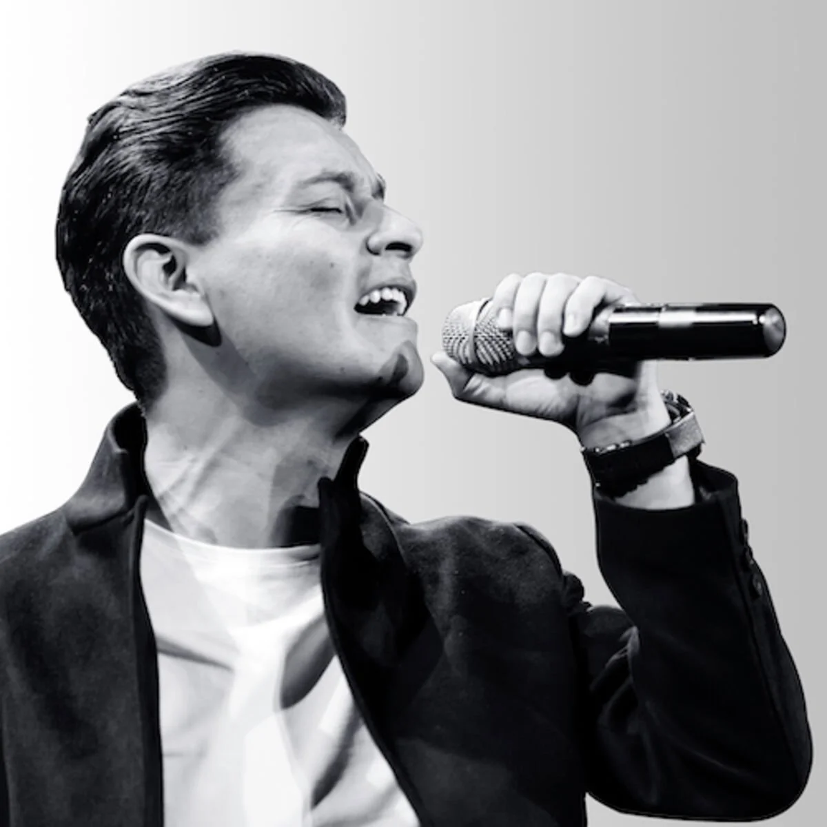 Hombre cantando o tocando un instrumento frente a un micrófono en un escenario oscuro con luces azules.