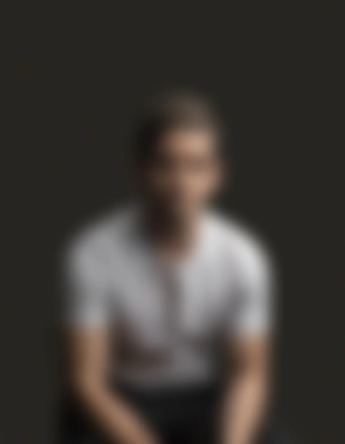 Persona con cabello castaño en un fondo oscuro, sonriendo y vestida con camiseta blanca.