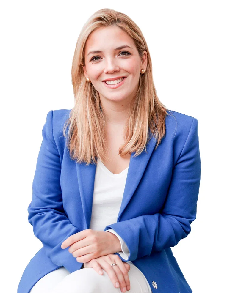 Mujer sonriendo, con cabello rubio y largo, vestida con blazer azul y blusa blanca, en fondo blanco.