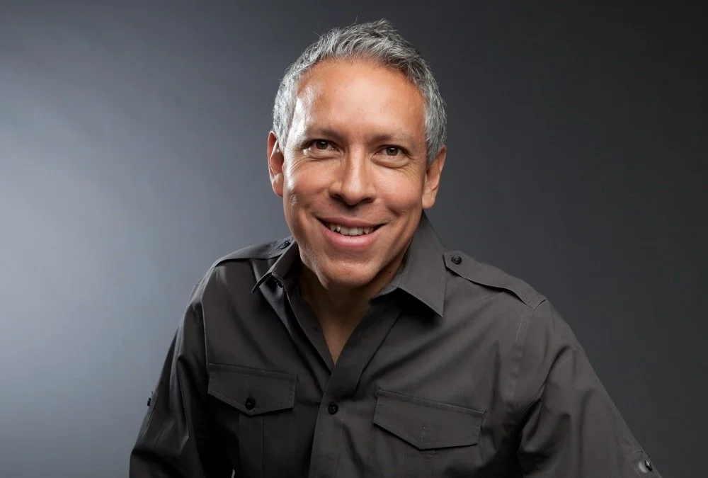 Hombre sonriendo, cabello canoso, camisa gris oscuro, fondo gris oscuro