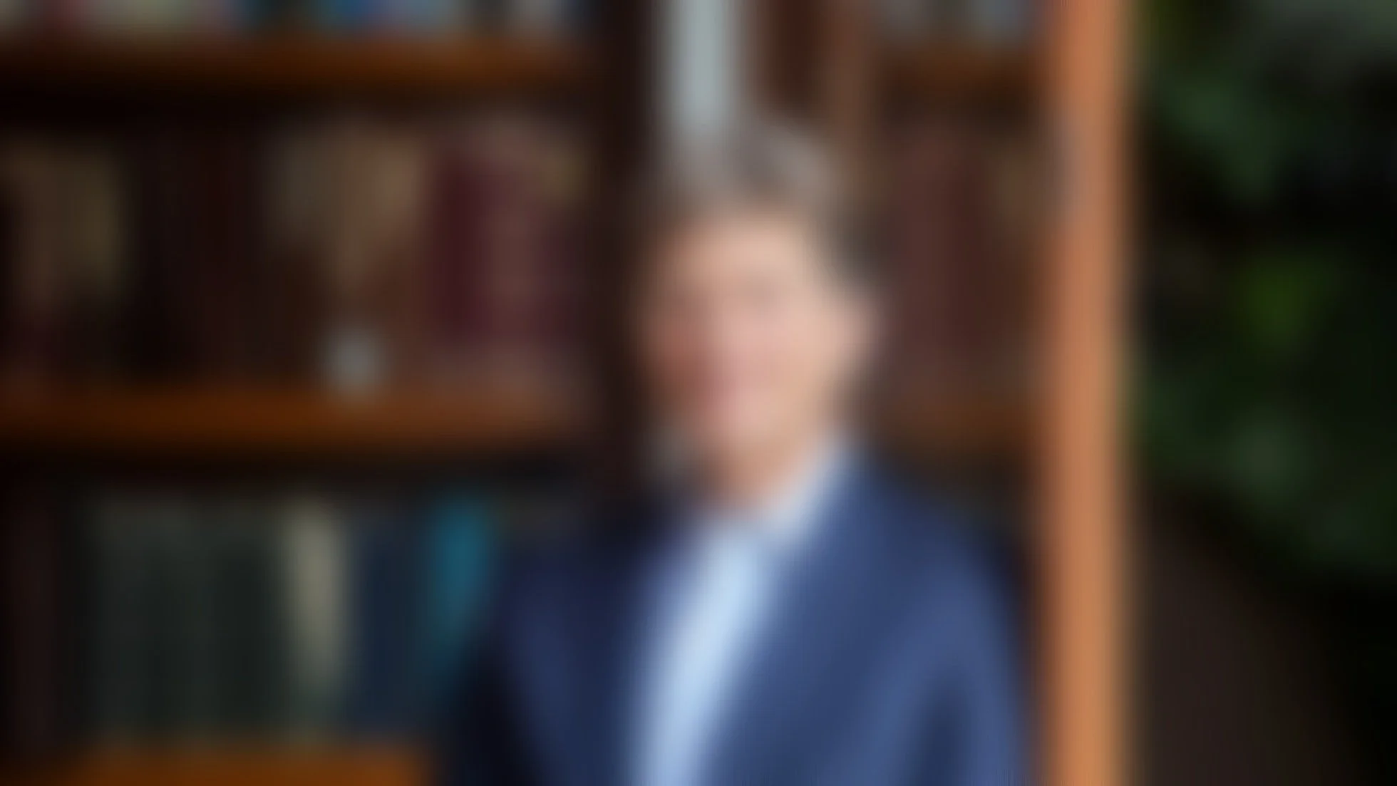 Foto borrosa de un hombre con traje azul, en un fondo de librerías de madera con libros.