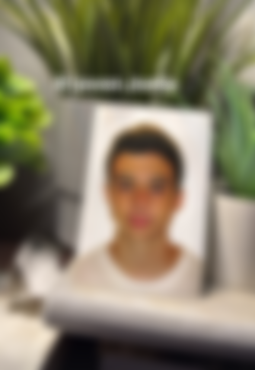 Retrato borroso de una mujer con gafas y cabello corto, observado desde un espejo o superficie reflectante, rodeada de plantas verdes.