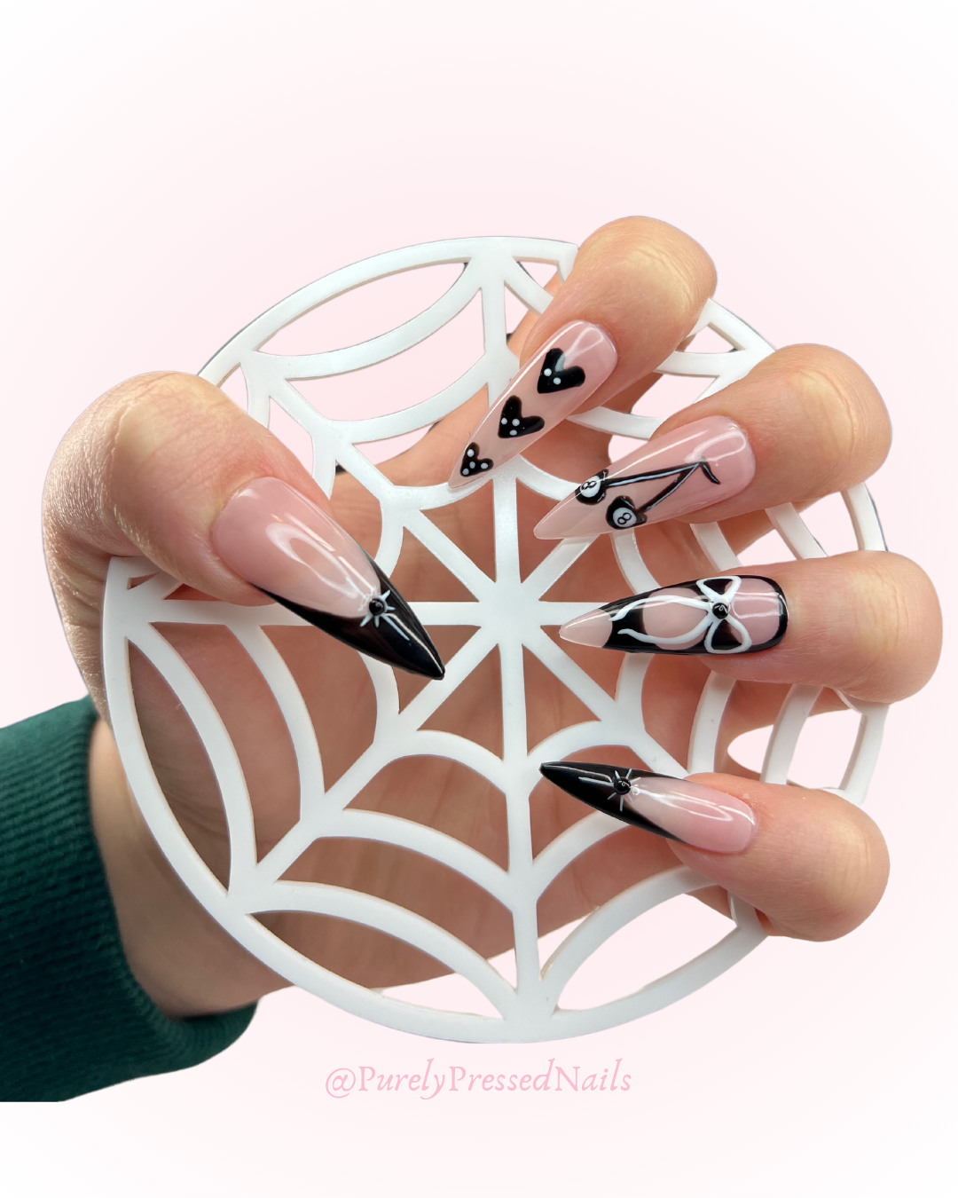 Hand with long almond-shaped nails featuring black and white designs, holding a decorative white web-like cutout.
