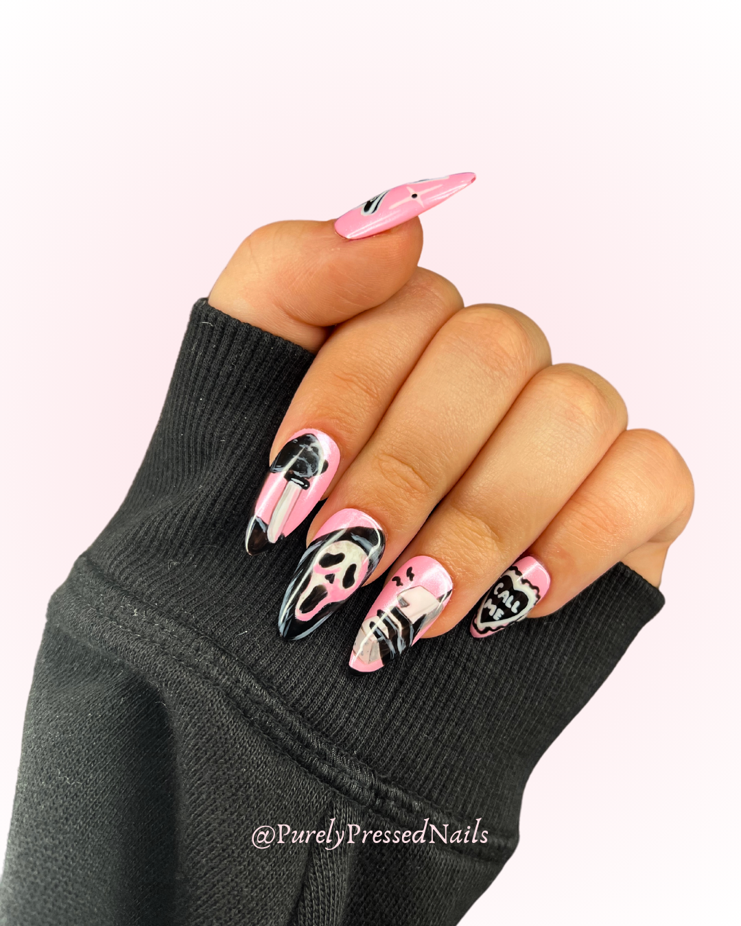 Nail art with black, white, and pink designs, including a skull, a speech bubble with 'CALL ME', and abstract patterns, on a person's hand with a black sleeve.