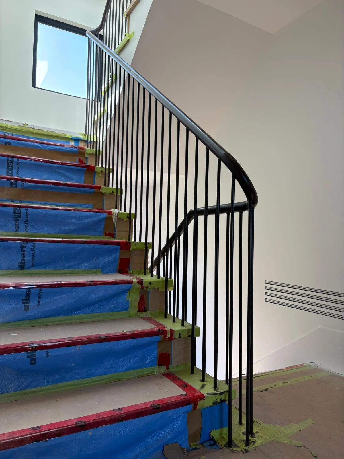 Custom interior railing installed around protected wood staircase finishes