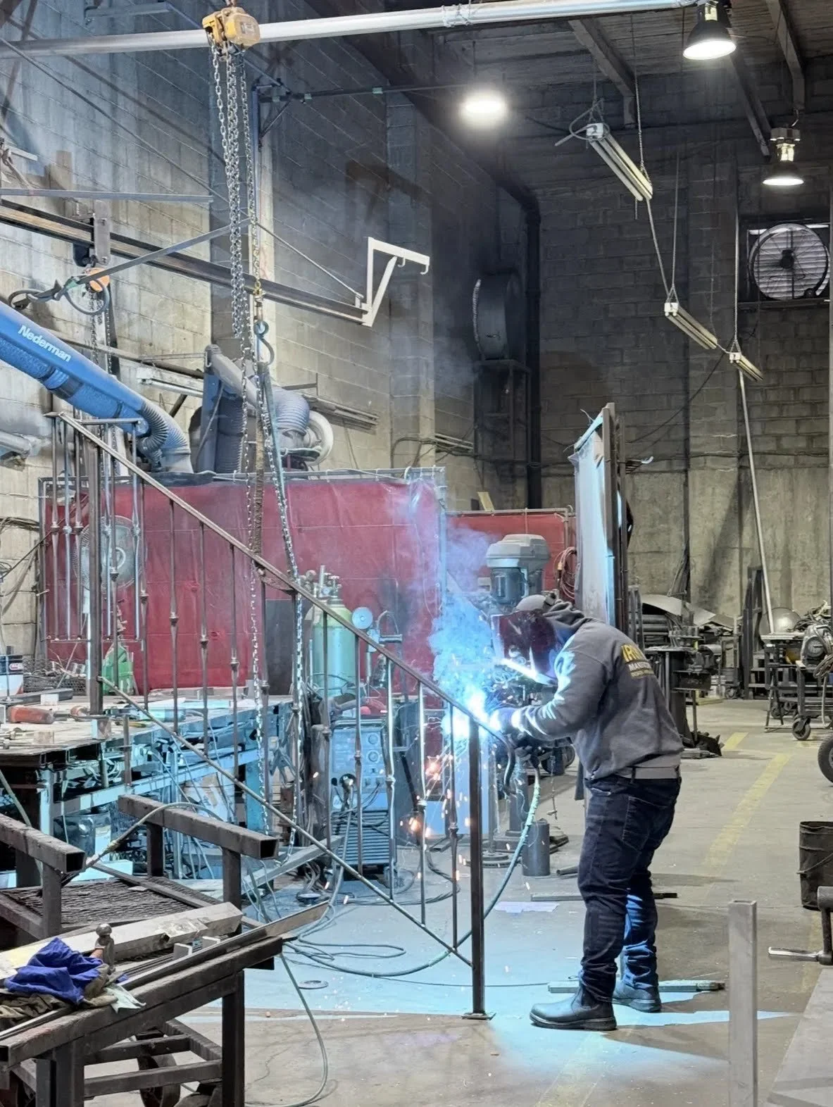 Welder assembling a custom metal railing in the Iron Age fabrication shop