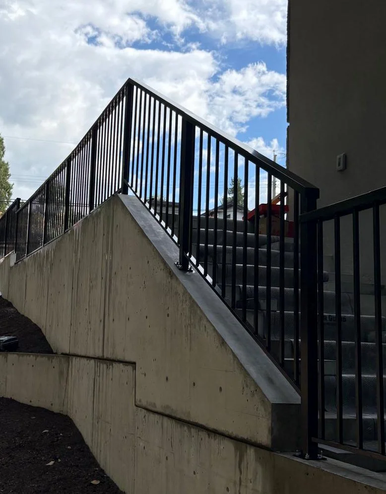 Custom black steel stair railing with vertical pickets installed along an exterior concrete staircase in Vancouver, BC.