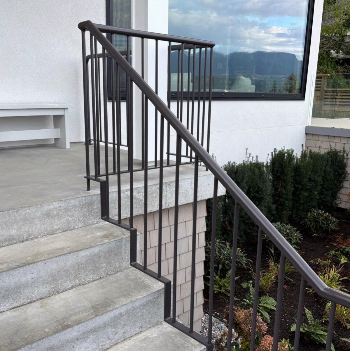 Finished exterior metal railing beside concrete entrance stairs and landscaping