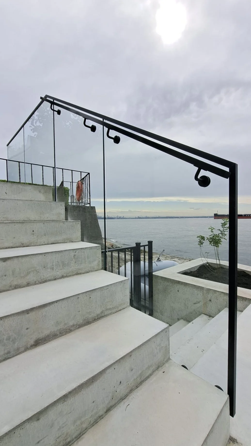 Custom exterior glass stair railing with black metal handrails installed on concrete steps in a modern Vancouver property.