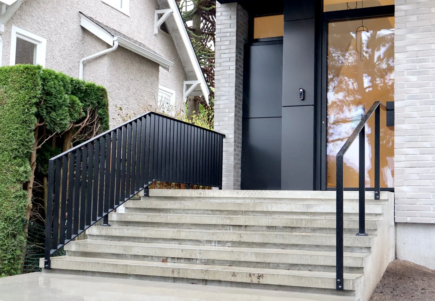 Modern exterior stairs with custom black metal railings for a residential entrance in Vancouver, fabricated by Iron Age Manufacturing.