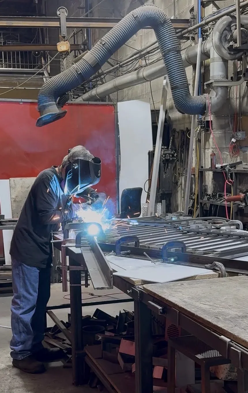 Welder assembling a custom metal railing in the Iron Age fabrication shop
