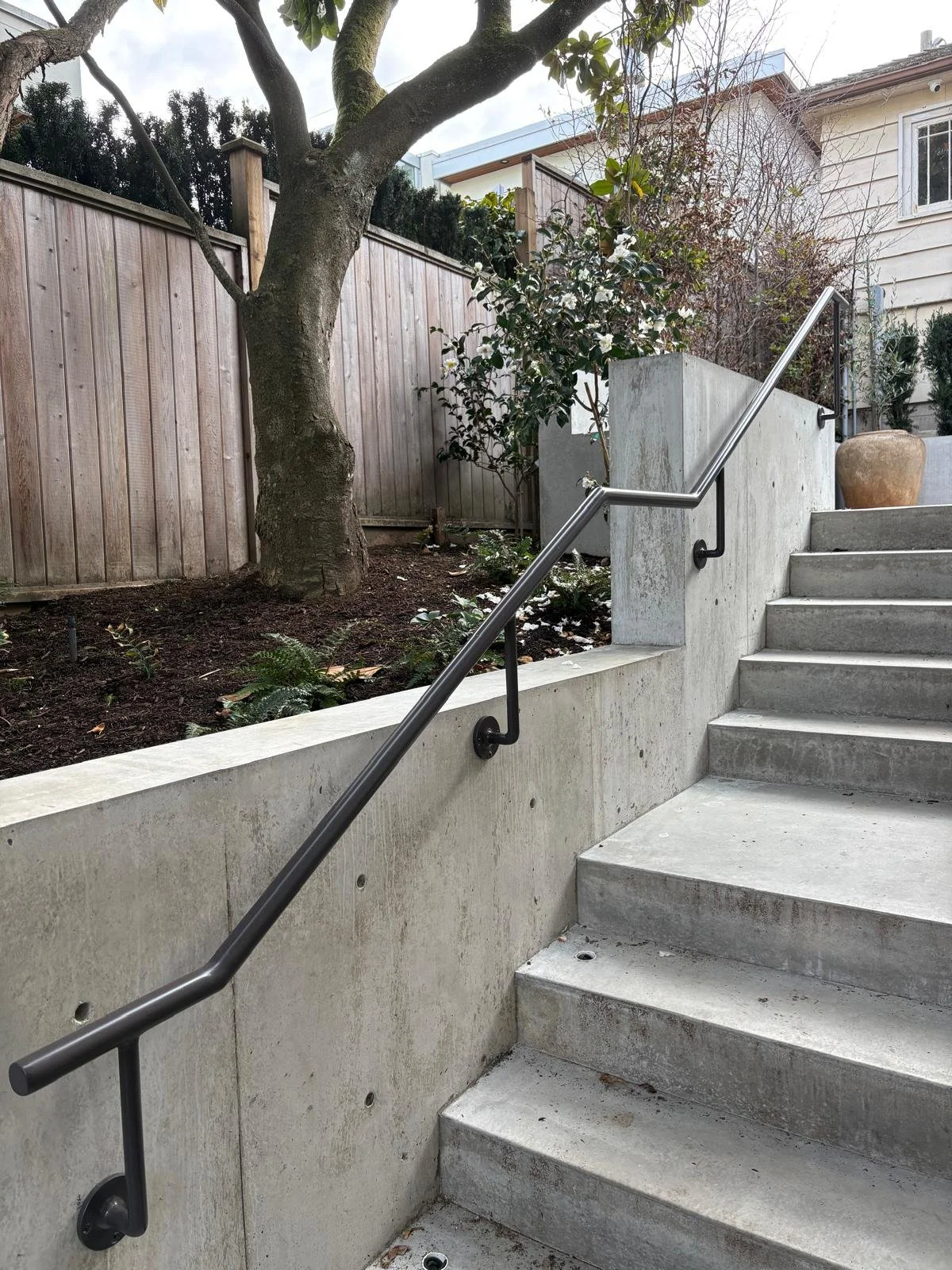 Wall-mounted metal handrail following exterior concrete garden stairs